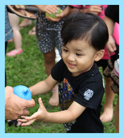 Little boy being given a blue water balloon.