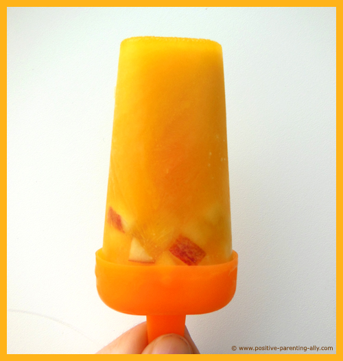 Orange juice lolli / popsicle with apple pieces as frozen snack for kids and toddlers.