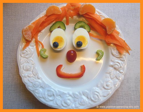 Funny face of vegetables and fruit on a plate as fun snacks for kids.Egg eyes, carrot hair, celery ears and bell pepper mouth. Great as raw snacks for toddlers. 
