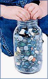 Toddler milestones of making things fit: Toddler hands making marbles fit into a jar.