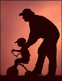 Silhoutte of father pushing little boy on his tricycle.