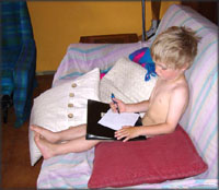 More concentration: Little boy sitting in sofa drawing.