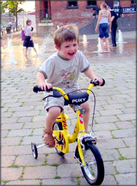 Child development stages of learning to bike and balance. Happy boy on bike with training wheels.