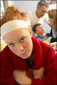 Adolescent development: Teen girl looking bored. Family in the background.